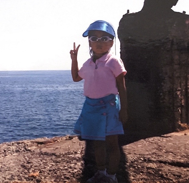 Childhood photo of Hazel making a peace sign on a coastal rock wall
